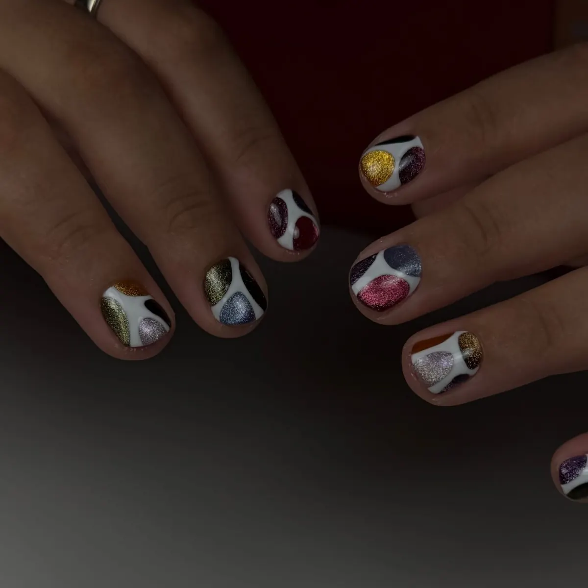 Uñas cortas, cada una pintada con un pequeño motivo multicolor distinto.