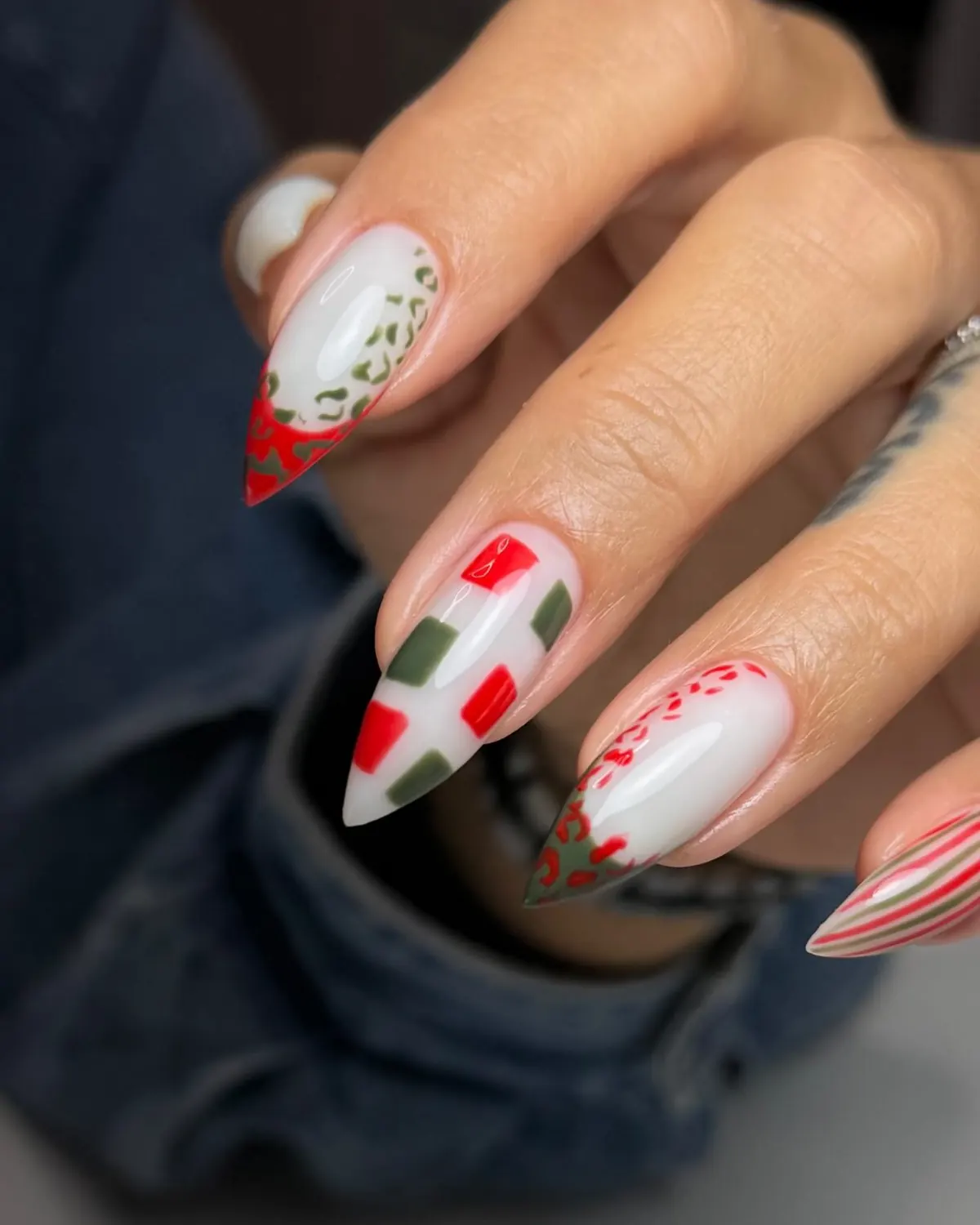 Primer plano de uñas almendra pintadas con cuadros y rayas rojas y verdes sobre blanco.